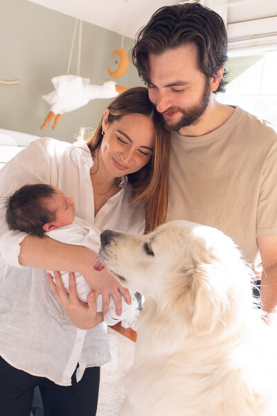 Charming family photo with a newborn lying on a blanket, gazing up at the camera while mom holds his hands and smiles.