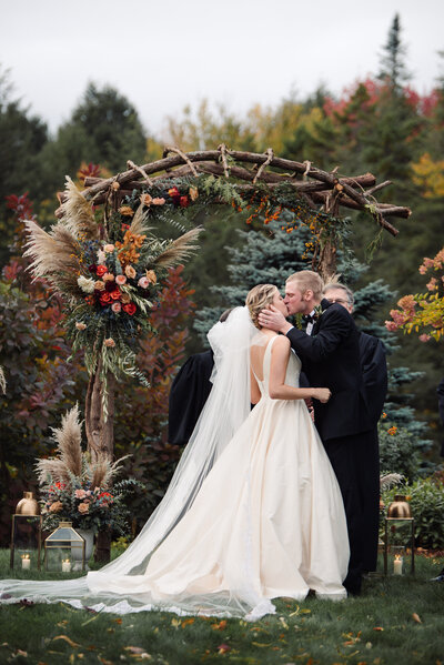 Colorful fall floral arch with formal wedding attire and romantic first kiss with Harlow and Dahlia events in Stowe VT
