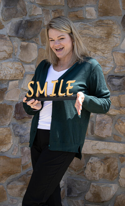 Kim Binkley posing for a headshot behind a rustic stone wall. 