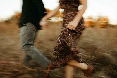 Guy and girl holding hands and running together in field at sunset in the fall