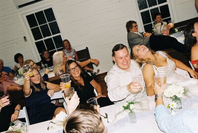 A table laughs while toasting at a rehearsal dinner