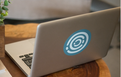 Laptop with orbital-themed sticker on wooden desk representing Brightspot CMS creativity and digital workspace
