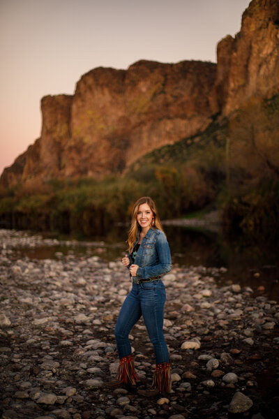 Makayla wearing a denim jacket and fringe cowboy boots standing in front of the salt river