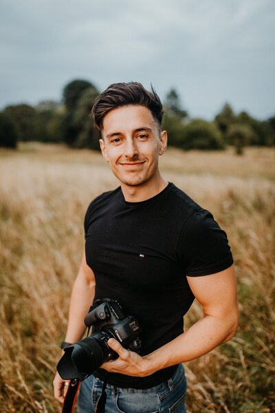 Headshot of Ollie Baines with camera in hand at outdoor photoshoot