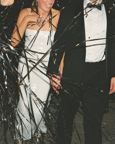 Film photo of bride and groom holding hands with silver streamers all around them