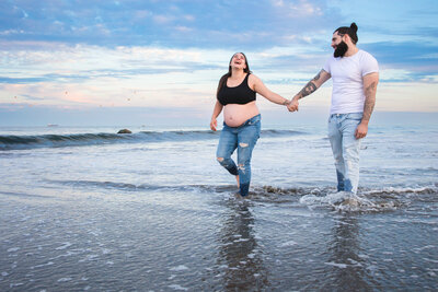 Expecting mother and father walking on the beach smiling at eachother