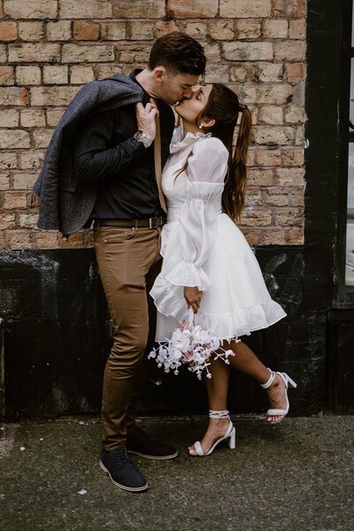 Bride and groom kissing by a brick wall