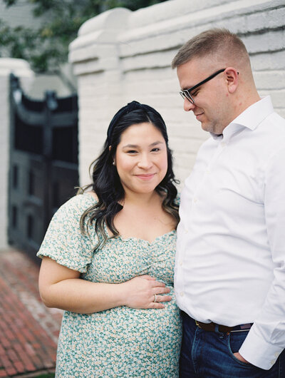 Portrait of a pregnant mother in a green dress holding her baby bump as her husband looks on by Richmond family photographer Jacqueline Aimee Portraits