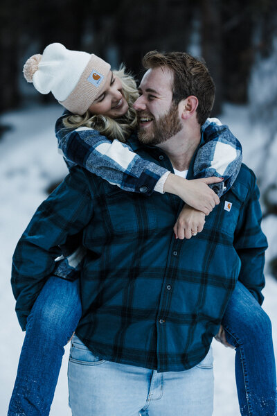 Wedding and Elopement Photography,  fiancé gives piggy back ride during snowy mountain engagement photos.