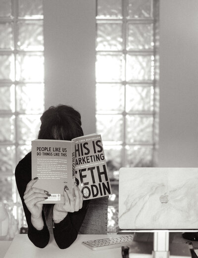 Keshia, a copywriter in Ireland, leans on a desk reading Seth Godin's This is Marketing