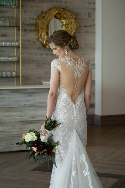 New England Wedding Photographer Pricing | Kelsey Sheehan Photography Timeless Rhode Island Weddings | Bride in an elegant lace wedding gown, holding a bouquet of white and red roses. She stands in a room with a gold mirror and wooden floors.