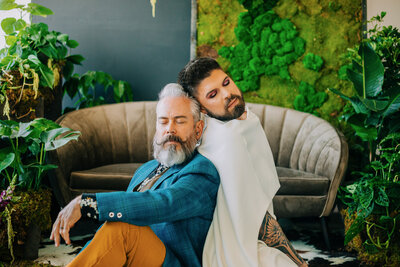 Two grooms sitting back to back with their eyes closed at Denver Photo Collective in Denver, Colorado, capturing a serene and intimate moment during their wedding photoshoot.