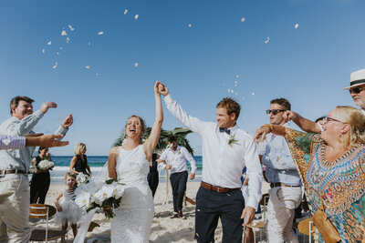 Happy, natural, fun, colourful wedding photograph on a NSW beach. Taken at Pacific Palms on the North Coast. Could be the Central Coast. Beautiful blue sky and celebrating couple after their wedding ceremony.