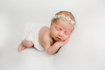 newborn girl laying on her side with leaf headband on white backdrop, ontario newborn photography studio