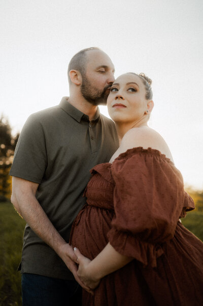 Expecting couple wrap each other up while holding the mother's baby bump in a gorgeous wildflower field. 