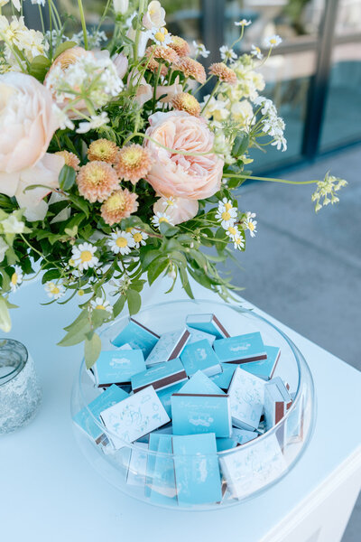 Custom calligraphy matchboxes sitting in a bowl at a wedding bartop featuring florals representing full service design and calligraphy by Life in Letters.