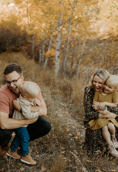 A mom and dad hug their son and daughter during a family session in the fall with fall leaves