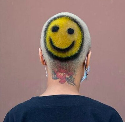 Image of hair salon client with short, bleached hair that has a yellow and black smiley face pattern dyed into the back of the head. 