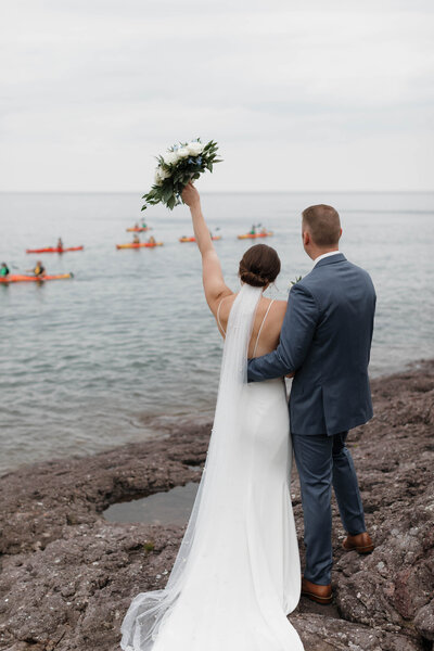 A newlywed couple celebrating as they look out at the water 