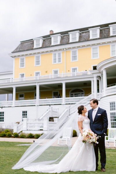 a bride and groom pose outside a grand house looking at eachother