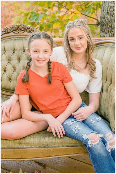 Two girls sitting on a green settee couch with fall leaves behind them in Campbellsville, Kentucky