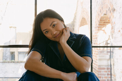 Indoor photographer brand photoshoot. Female photographer sitting, resting hand on face