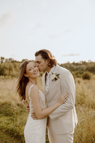 Bride poses in floral wedding dress in a a field while its raining