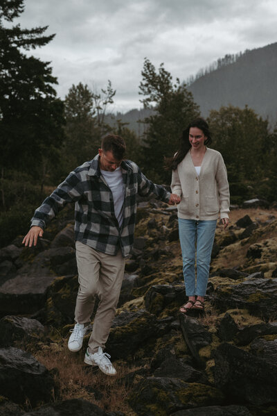 Couple photo session in the Columbia River Gorge. They are holding hands walking on unbalanced rocks.