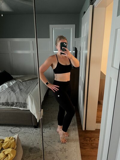 Women taking a mirror picture of her in athletic clothes showing her transformation after working out consistently to Fit by Coach Kel
