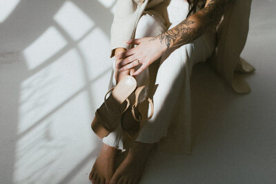 close of up of woman with floral tattoos sitting on the floor holding nude heels