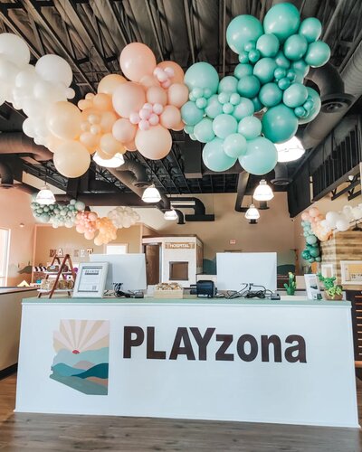 Indoor pastel balloon ceiling installation in soft mint, peach, and white colors above a cozy lounge area with beanbags and modern décor.