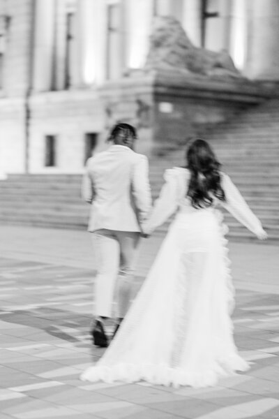Out of focus black and white photo of a bride and groom from the back walking hand in hand.