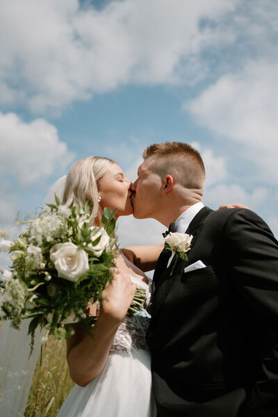 Bride and groom posing under a blue sky with fluffy clouds at willowbrook