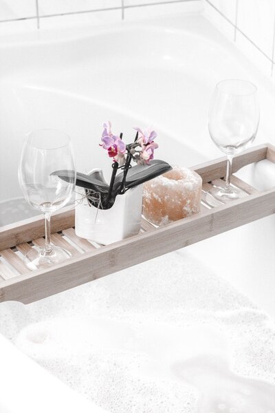 spa tray holding small plant and two win glasses over a white tub