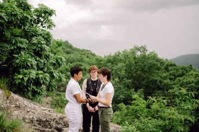 Bride and groom standing hand in hand with a mountain lake behind them during their intimate Virginia elopement, photographed in natural light and soft tones.

