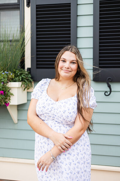 Senior girl smiles at camera in front of blue house in Portsmouth, New Hampshire