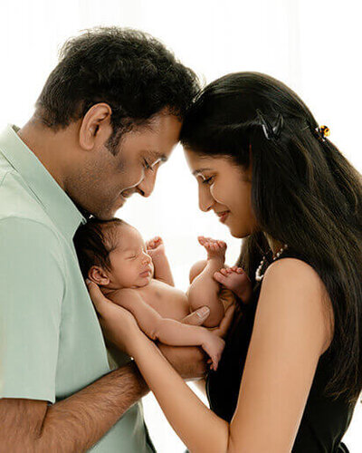 A father and mother holding their newborn with white light behind them.