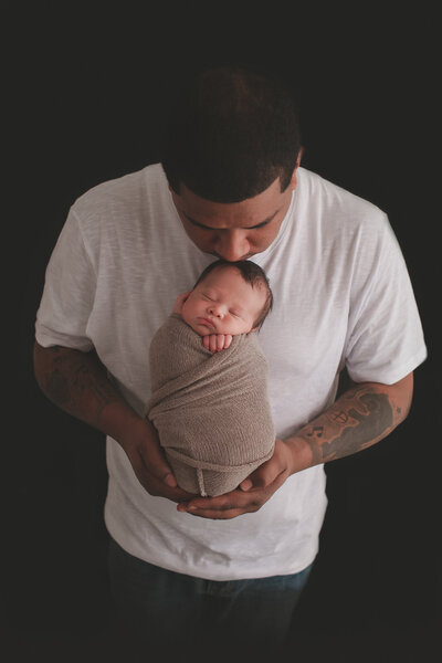 newborn baby boy wrapped in swaddle with dad holding him and kissing head