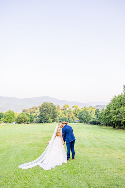 bride and groom kissing in a field with mountains in the background at Laurel Ridge Country Club