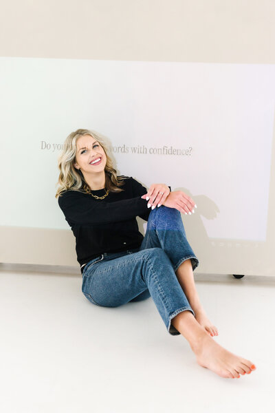 Sarah Klongerbo sitting on a leather couch holding a magazine in front of her face