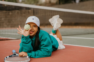 teen holding tennis ball and tennis racket on field