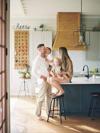 Family of four sitting on the kitchen counter together smiling at each other
