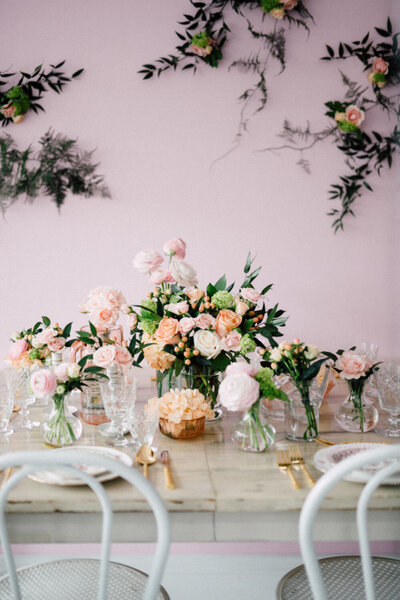 Floral table arrangement with pink and peach flowers against a pastel wall
