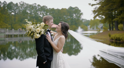 Bride and groom smile at each other in front of a lake