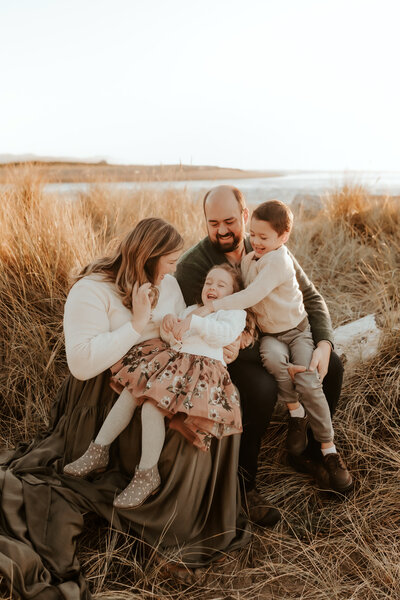 Hope Louise and her family sitting at the beach in fall outfits.