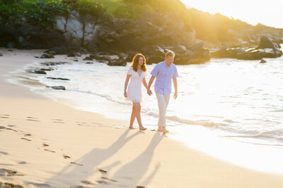 Couple Holding hands while walking with a gorgeous sunset lighting at Kapalua Bay captured by Maui Photographer Mariah Milan.