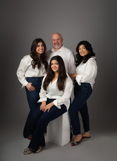 Casual family portrait with a formal lighting setup in studio, Dad, mom and 2 daughters on grey backdrop with white shirts, jeans and fancy shoes.