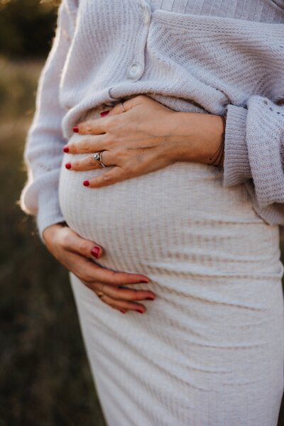 Frau die Hände auf Babybauch hält bei einem Outdoor Fotoshooting