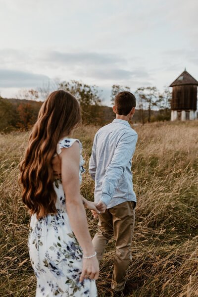 Engaged couple hand-in-hand, walking through a lush field in Pawling, capturing their love and the natural beauty of their engagement session.