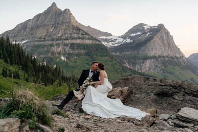 A couple sits on a rock at an overlook in Glacier National Park on their elopement day,